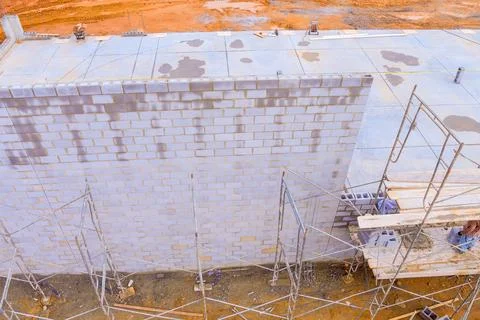 At construction site, mason makes concrete walls with cement blocks while 写真素材