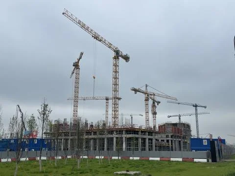Construction site with multiple cranes and building in progress on a cloudy d Stock Photos