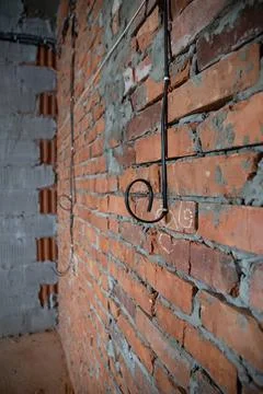 Construction site, one electric wire runs down a brick wall in a room Stock Photos