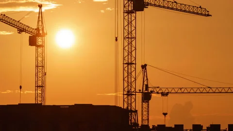 Construction site at orange sunset. Silhouette of high tower cranes works on Stock Footage 160390599
