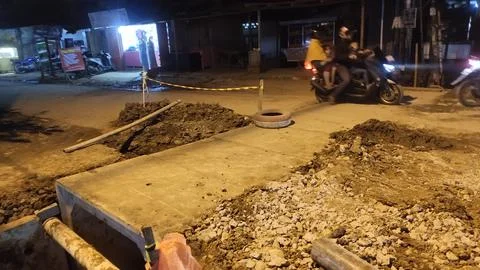 A construction site with a partially completed road and motorbikes passing by Stock Photos