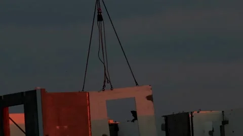 Construction site with pre-fabricated wall panel being lifted by crane against Stock Footage 325298179