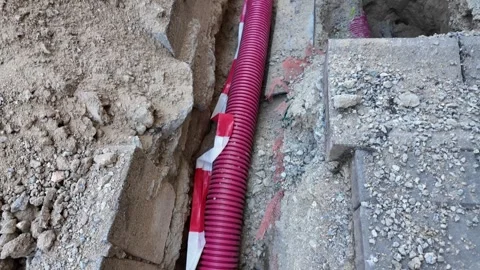 Construction site with red conduit pipes and warning tape in excavated trench Stock Footage 339290161