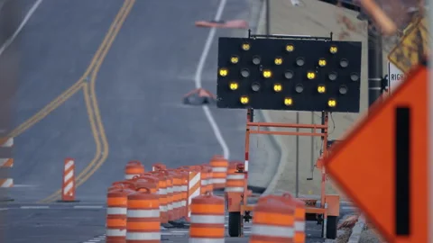 Construction site on road, flashing arrow sign to redirect traffic, telephoto Stock Footage 242880646