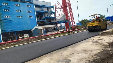 Construction site with a road roller paving asphalt near industrial buildings Stock Photos