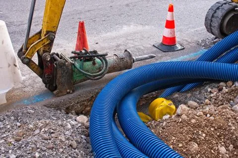 Construction site, road work. Hydraulic crushing hammer. Plastic pipes for el Stock Photos
