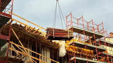 Construction site with scaffolding up, crane moving structural elements up Stock Footage 326278040