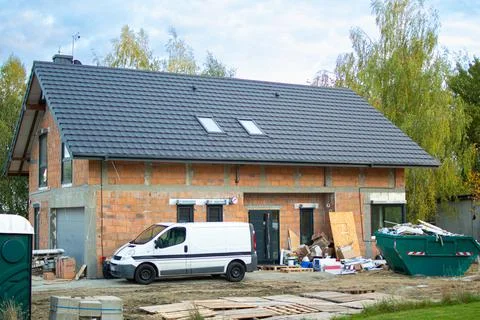 Construction site showing a partially built house with a white van and dumpster Stock Photos