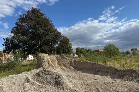 A construction site is shown with a large mound of gravel and a tree Stock Photos