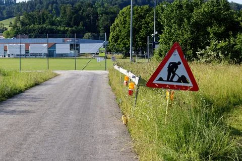 Construction site sign next to a through road and green meadow Stock Photos
