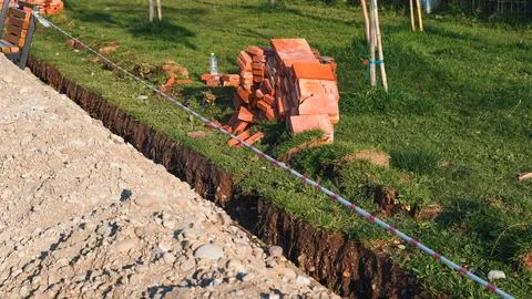 Construction site with stacked bricks and excavated trench in grassy area Stock Photos