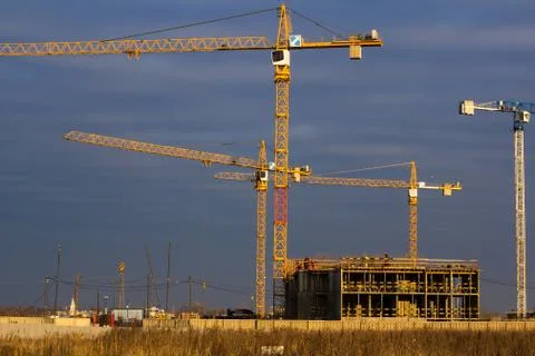 Construction site with tower cranes in a field against a dark blue sky Stock Photos