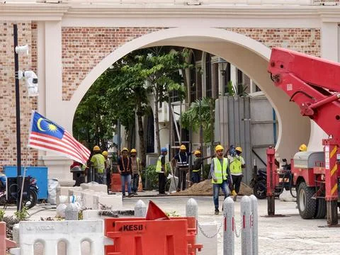 Construction Site Under Archway With Workers, Flag, and Heavy Equipment Stock Photos