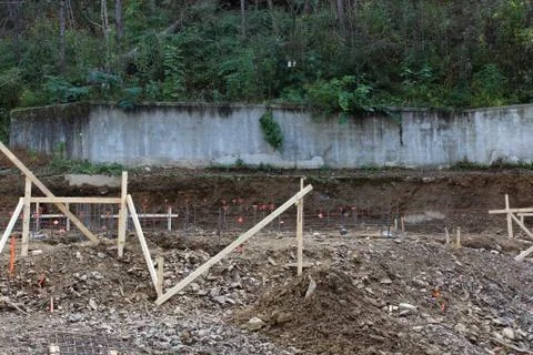 Construction site view of concrete retaining wall behind dug footings and rebar Stock Photos