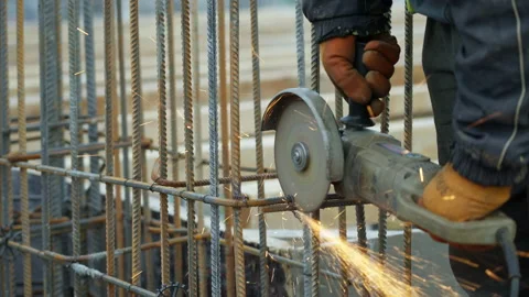 A construction site worker wearing protective gloves uses an angle grinder and Stock Footage 155835803