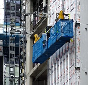 Construction Site Workers In Cradle Workig On Building Stock Photos
