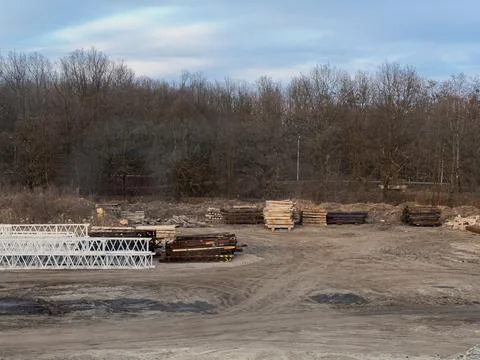 A construction site yard filled with stacks of metal beams, wooden planks, and Stock Photos