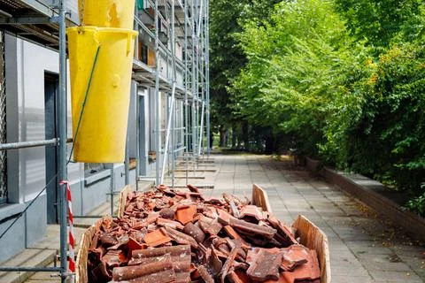 Construction skip bin filled with old roof tiles under a yellow debris chut.. Stock Photos