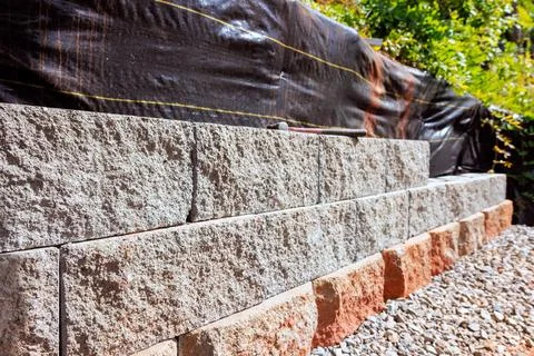 Construction of stone wall using gray orange blocks in garden area 스톡 사진