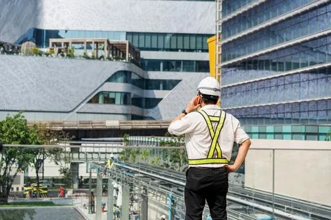 Construction supervisor talking on smartphone while coordinating workers an.. Stock Photos