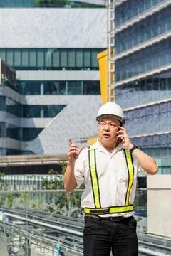 Construction supervisor talking on smartphone while coordinating workers an.. Stock Photos