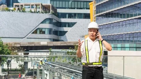 Construction supervisor talking on smartphone while coordinating workers an.. Stock Photos