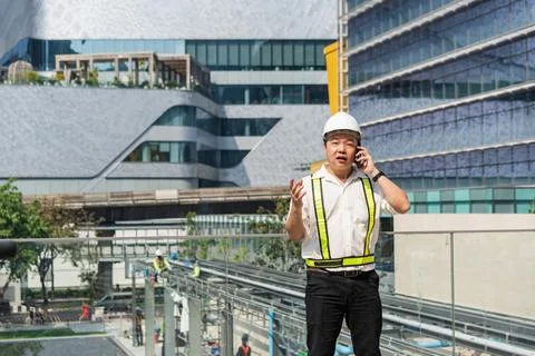 Construction supervisor talking on smartphone while coordinating workers an.. Foto stock
