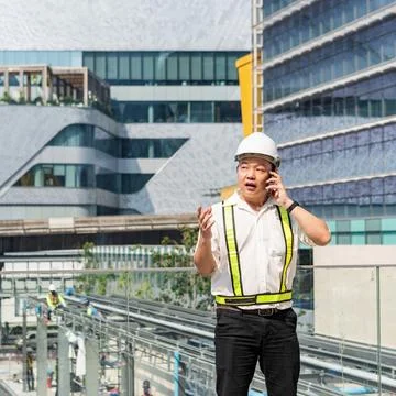 Construction supervisor talking on smartphone while coordinating workers an.. 库存照片