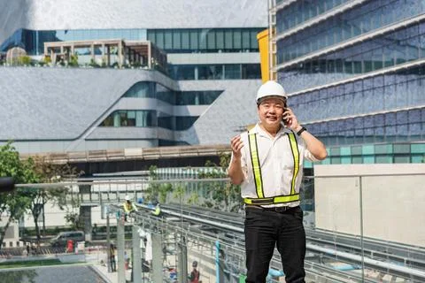 Construction supervisor talking on smartphone while coordinating workers an.. Stock Photos