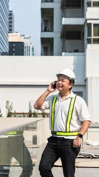 Construction supervisor talking on smartphone while coordinating workers an.. 스톡 사진