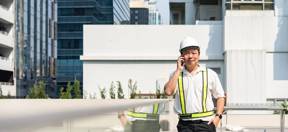 Construction supervisor talking on smartphone while coordinating workers an.. 库存照片
