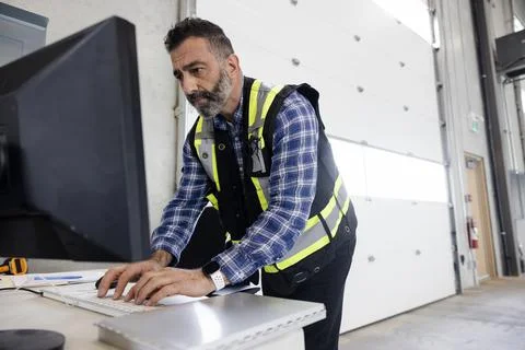 Construction supervisor working on computer on desk in warehouse Stock Photos