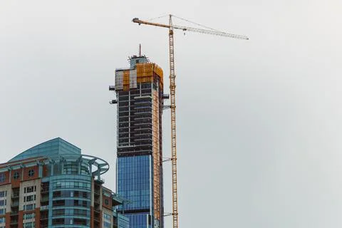 Construction of tall building with crane at work in urban area during daytime Foto stock