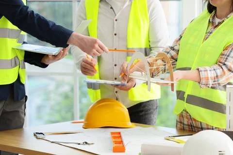 Construction team collaborating on a bridge model with blueprints and safety  Stock Photos
