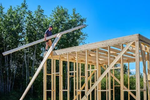 Construction of timber frame house, young worker lifts long wooden boards t.. Stock Photos