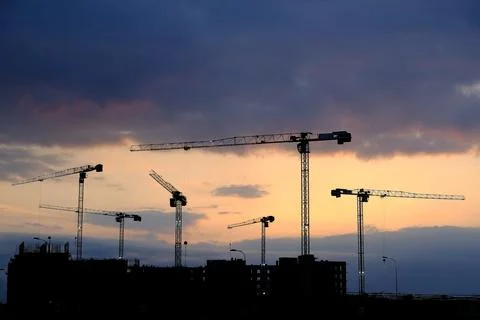 Construction, tower cranes are working on the background of the sunset. Stock Photos