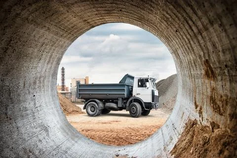 A construction truck is parked inside a large concrete pipe at a building sit Stock Photos