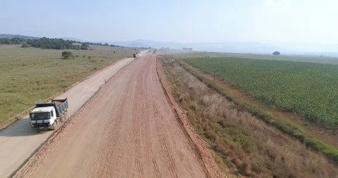 Construction trucks pass under camera flying over road being built in rural Stock Footage 85955986