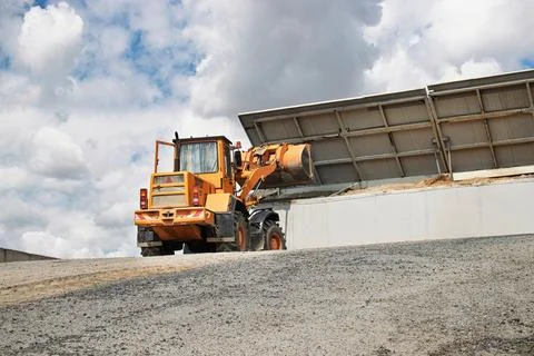 Construction vehicle unloading materials at a work site under a cloudy sky Photos