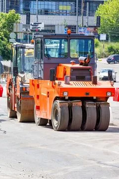 Construction vehicles work on a road project in a busy city area during the d Stock Photos