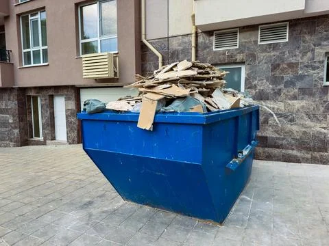 Construction waste is collected in a large blue dumpster outside a building.. Stock Photos