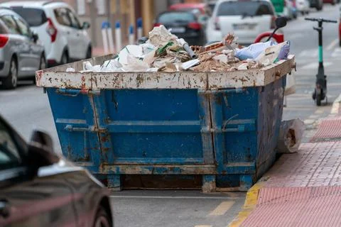Construction waste dumpster container on urban street sidewalk Stock Photos