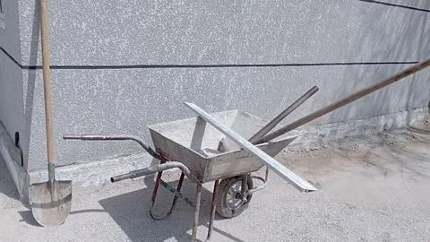 Construction wheelbarrow-trolley rake, pitchfork inside. Shovel stands against Stock Photos