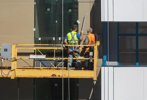 A construction winch with workers sealing joints between the facade panels Stock Photos