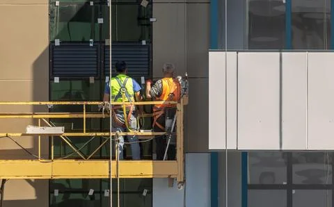 A construction winch with workers sealing joints between the facade panels Stock Photos
