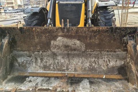 Construction work happening with a loader bucket on a dirt site in a city area Stock-Fotos