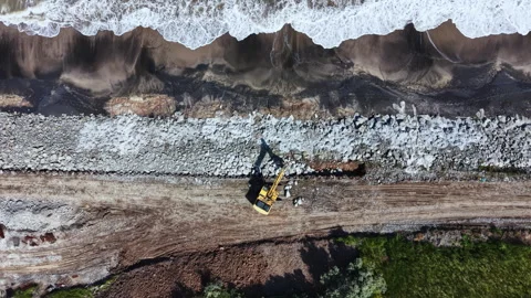 Construction work occurs on a beach as waves crash along the shore in a coastal Stock Footage 337917353