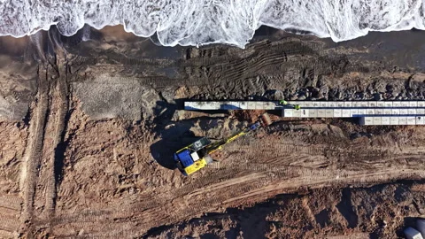Construction work takes place on the beach where workers use heavy machinery to Stock Footage 331334831