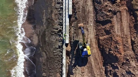 Construction work takes place on the beach during daylight hours while machines Stock Footage 331334924