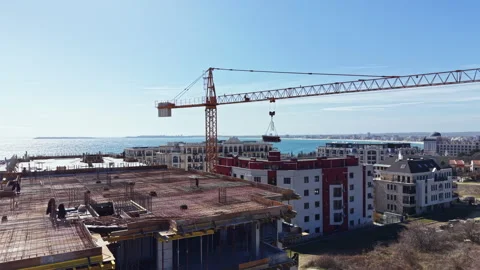 Construction work takes place at a building site near the water during a sunny Stock Footage 331331349